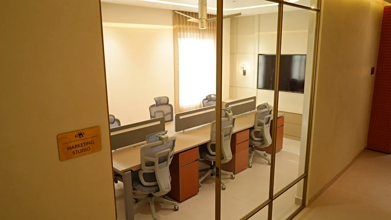 Glass-fronted marketing studio with partitioned desks and a wall-mounted screen