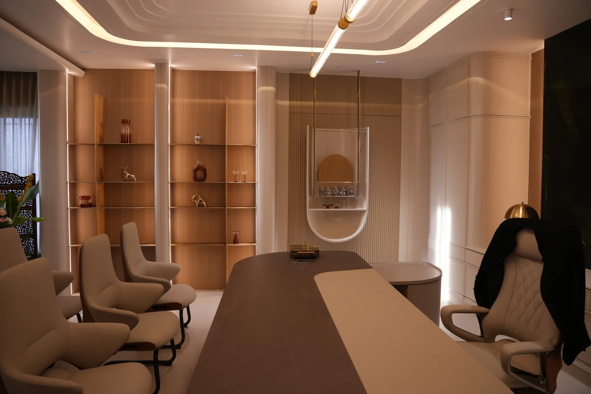 Office room with a large desk, upholstered visitor chairs and illuminated display shelves