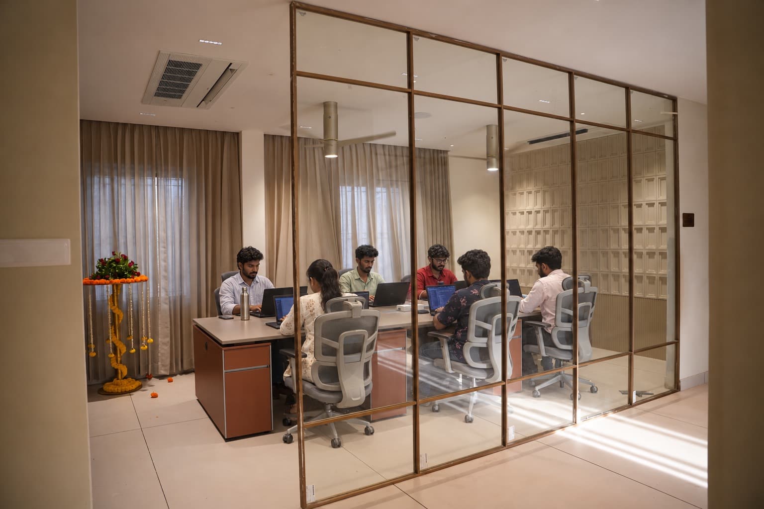 Team members working at laptops in a glass-walled office