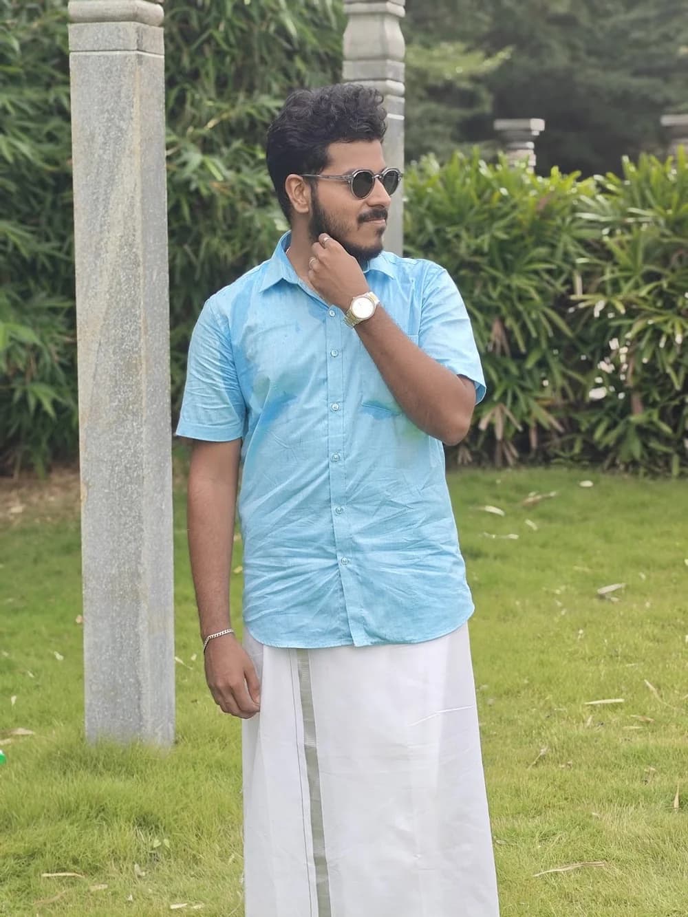 Team member in a blue shirt and white traditional attire standing in a garden