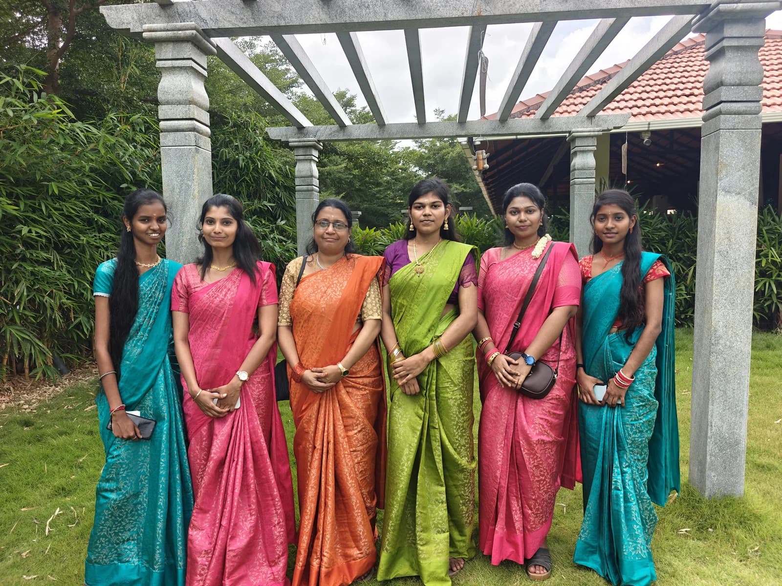 Six team members in colourful saris standing beneath a stone pergola